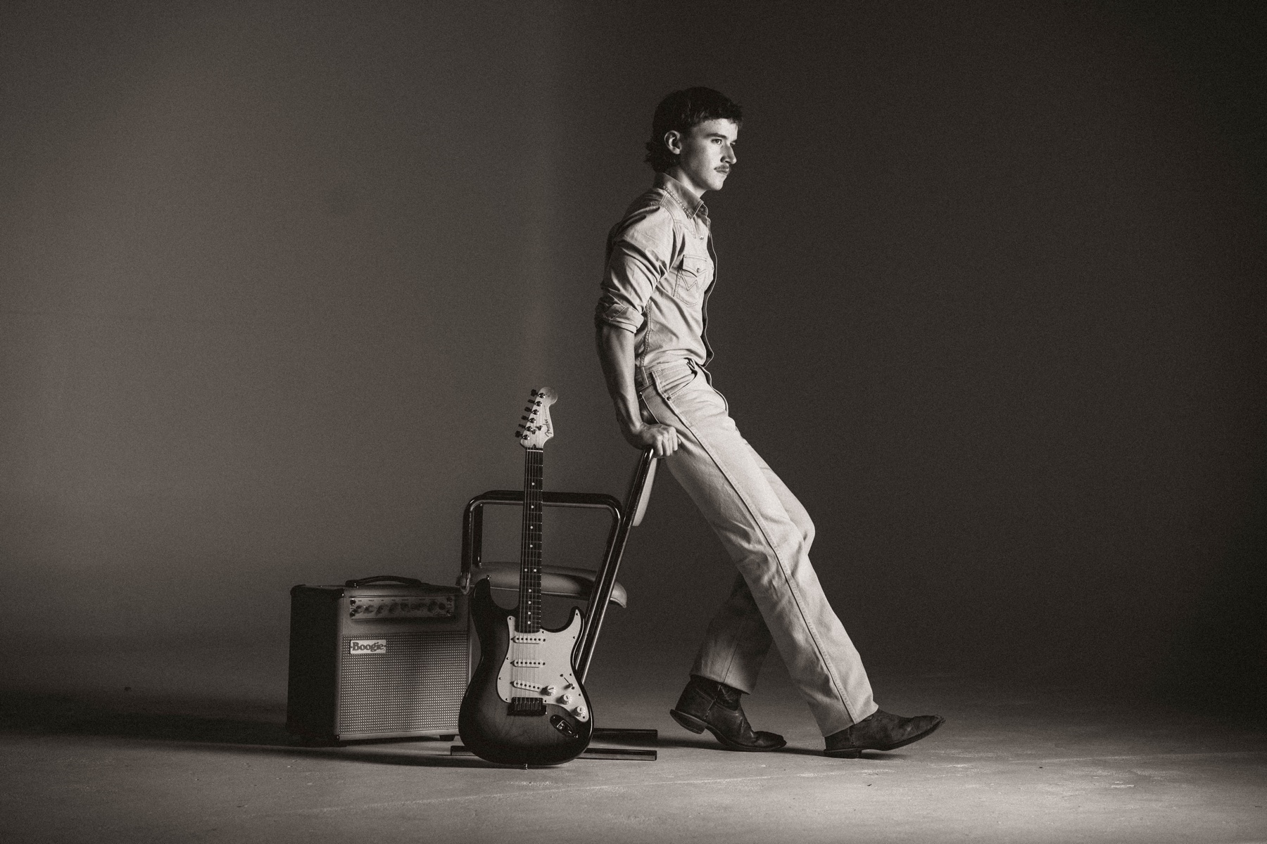 Black-and-white portrait of Phil Kane leaning against a chair beside an electric guitar and amplifier