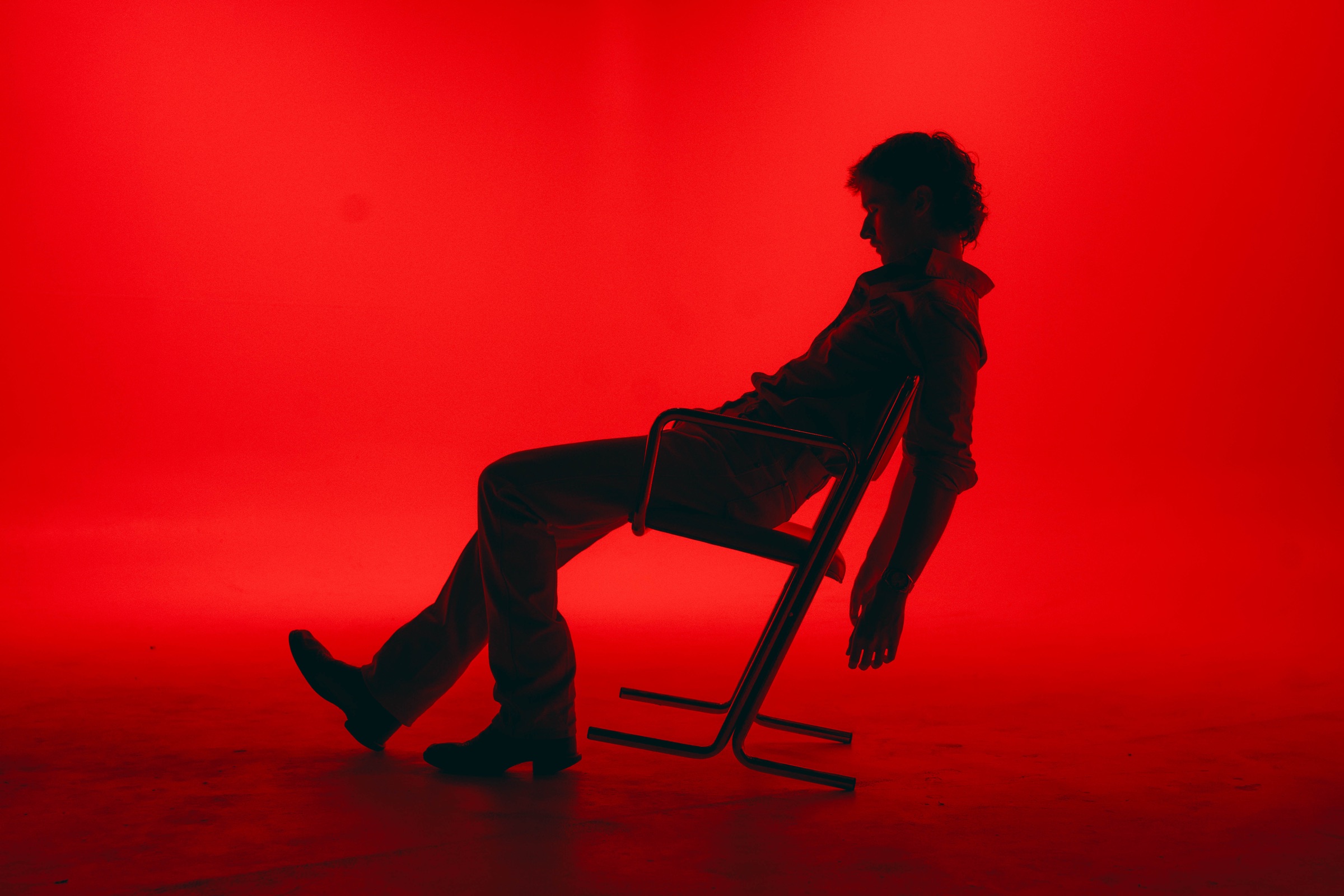 Phil Kane leaning back in a chair against a vivid red studio backdrop