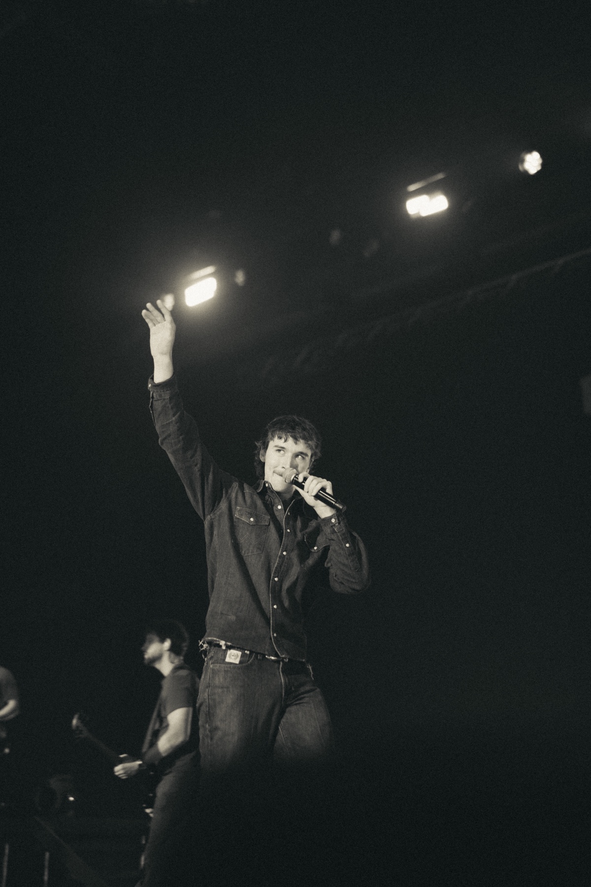 Phil Kane raising one hand to the crowd while singing into a handheld microphone